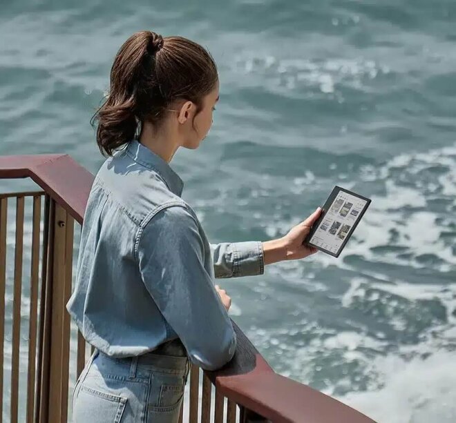 Copy electronic vam predstavlja Tablet Onyx Boox Go Color7(Gen II) 7″ eTablet, Wifi, Bluetooth,OBGC7G2. Na fotografiji je djevojka koja stoji na terasi sa pogledom u more. U ruci drži tablet i čita.