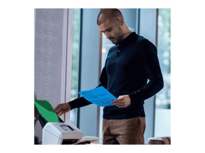Copy electronic vam predstavlja Skener BROTHER ADS-4900W Professional Desktop [ADS4900WTF1]. Na fotografiji je muškarac u radnom prostoru a ispred njega je skener. Skener je postavljen na radnu policu. Zeleni list papira je na skeneru u ADF-u a plavi papir drži muškarac.
